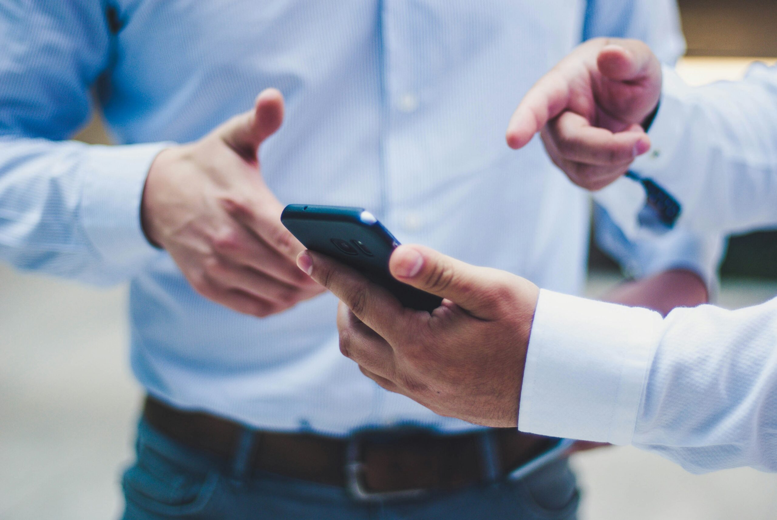 Eine Hand hält ein Smartphone, zwei weitere gestikulierende Hände